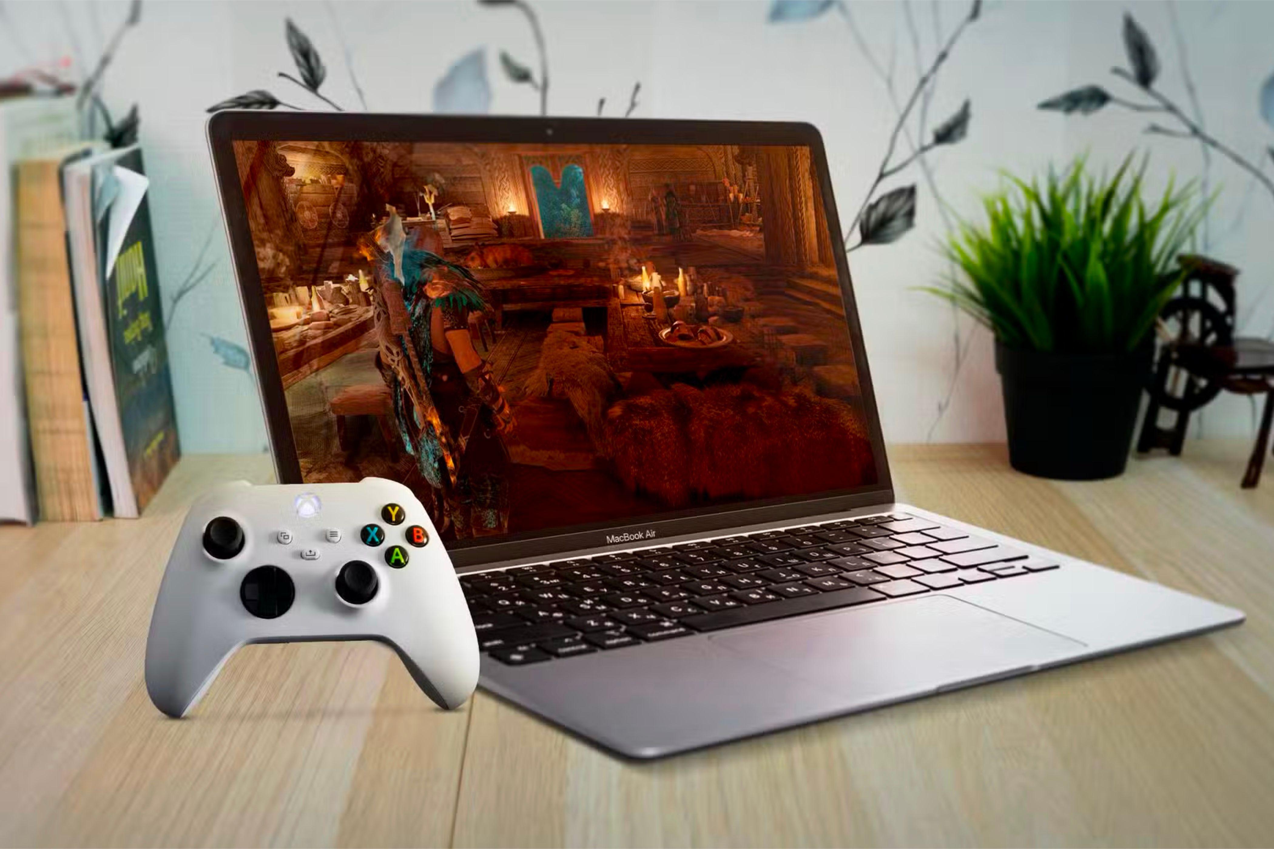 How to Set Up a Mac for Better Gaming: Optimize in 4 Simple Steps ⚡✨ 10 A MacBook Air under a wooden table with a game on the screen and an Xbox controller to the left.