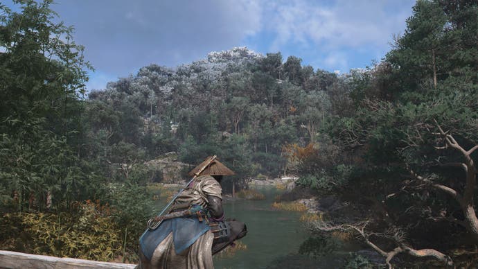 Screenshot da AC Shadows che mostra Naoe appollaiato su una recinzione sopra un lago e una foresta
