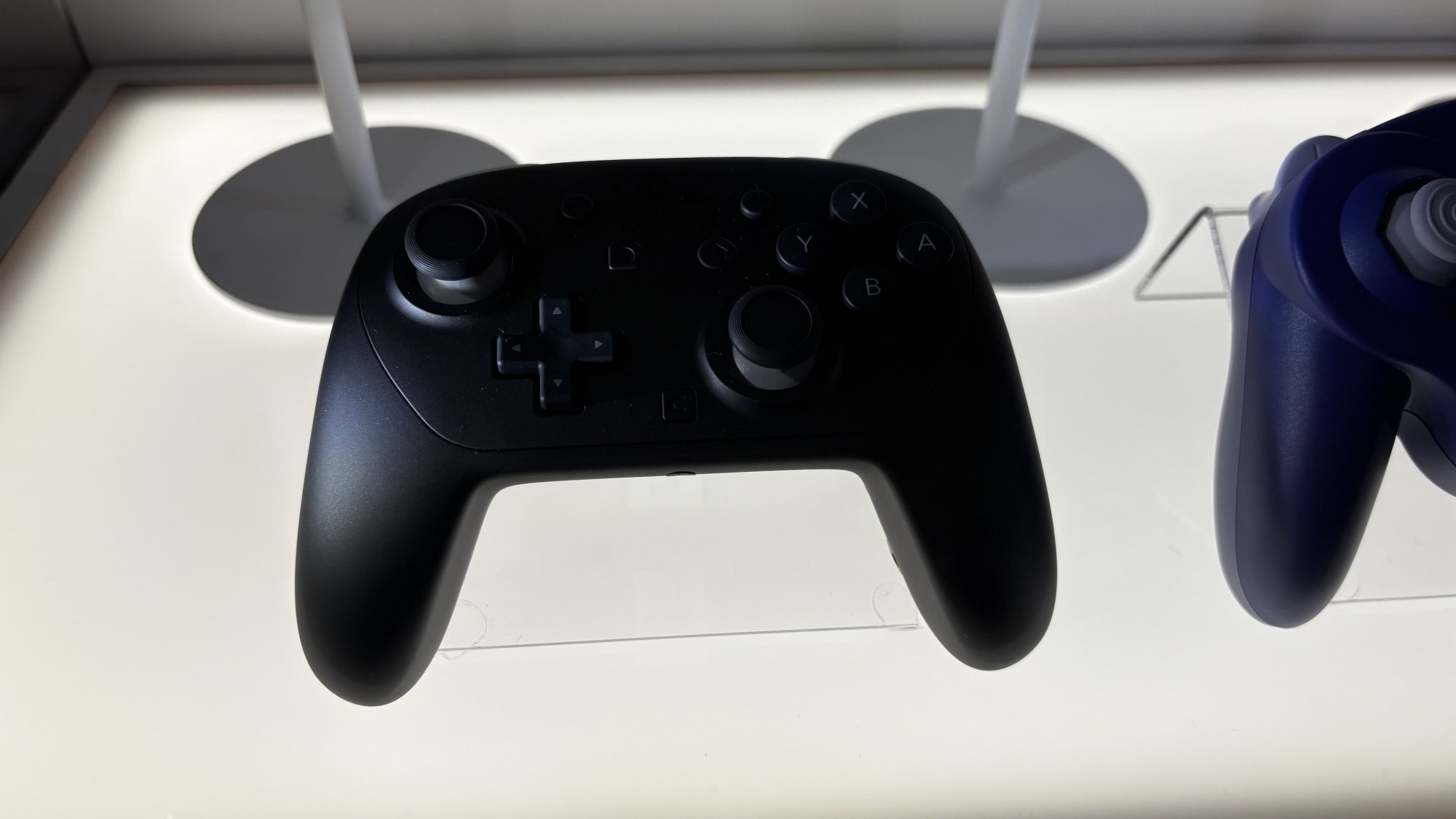 Switch 2 vs Switch 1: +FPS y pantalla 120Hz. 8 Pro Controller de Nintendo Switch 2 detrás de una vitrina