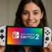 Switch 2 против Switch 1 — человек держит белую портативную консоль Nintendo Switch 2 с логотипом на экране, иллюстрируя сравнение дизайна Switch 2 и Switch 1.